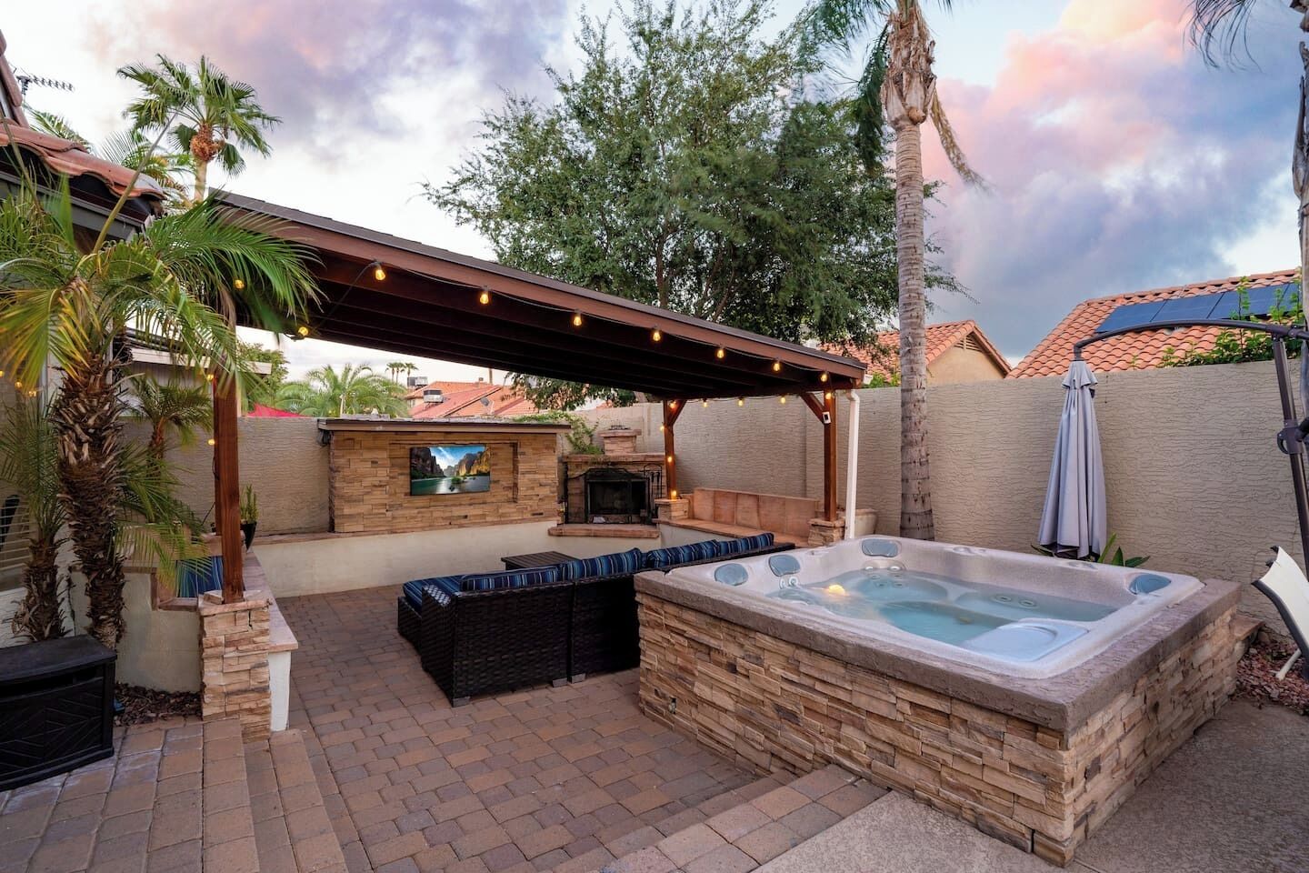 A backyard with a hot tub, outdoor seating, a fireplace, and a pergola with string lights.