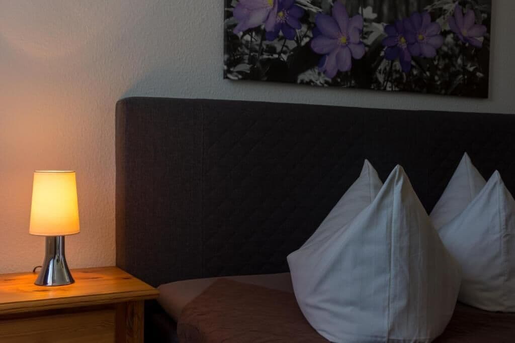 A neatly made bed with white pillows, a bedside lamp, and a floral painting on the wall.