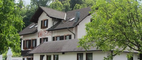 A two-story building with a tiled roof, a sign with text, and a stone wall in front.