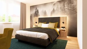 Un dormitorio moderno con una cama grande, una mesita de noche, una silla y un mural en la pared con un bosque.