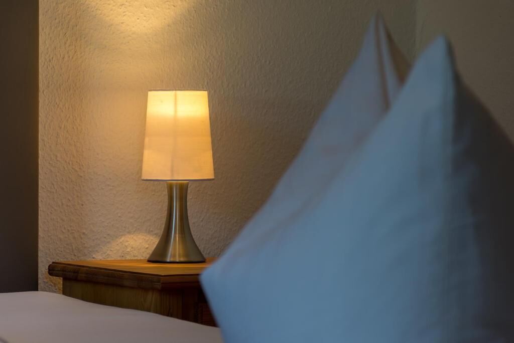 Une lampe de chevet posée sur une table de nuit en bois, à côté d’un lit.