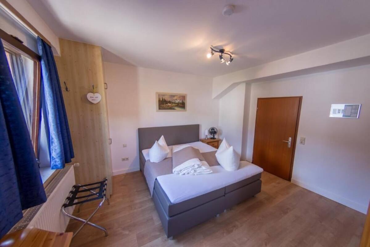 Un dormitorio con cama, un radiador, una ventana con cortinas, una puerta y una lámpara fijada a la pared.