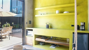 A bright yellow kitchen with shelves holding dishes, a coffee maker, and a potted plant. - The Sandhaus Suite 3 (Jacó)