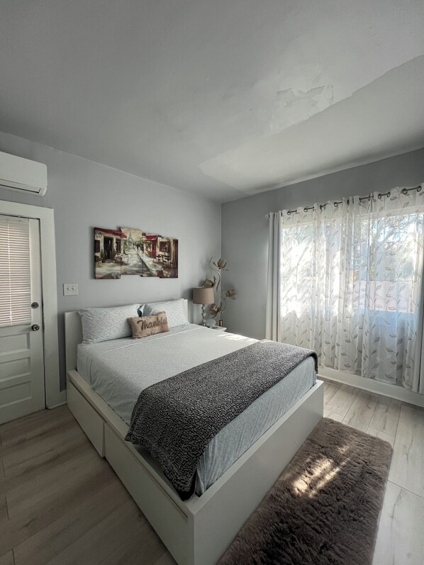 Une chambre à coucher avec un lit, un tableau, une lampe et une fenêtre avec des rideaux.