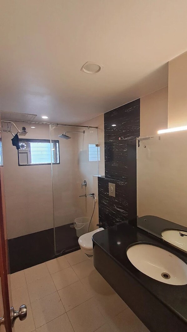 A modern bathroom with a glass shower enclosure, a white toilet, and a black vanity with two sinks.