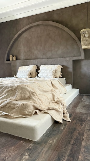 Ein Bett mit hohem Kopfteil, einer gewobenen Leuchte und einem Holzboden.
