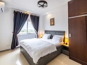 Moderni hotellihuone, jossa on suuri sänky, tummat verhot, yöpöytälamppu ja vaatekaappi.