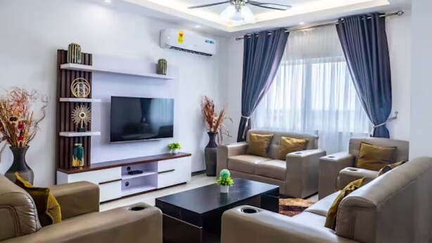 A modern living room with a flat-screen TV, comfortable sofas, a coffee table, and decorative items. - Luxurious Getaway: 24/7 Security - Pool - Balcony! (Sakumono)