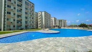 A modern apartment complex with a central swimming pool and a paved walkway. - Luxurious Getaway: 24/7 Security - Pool - Balcony! (Sakumono)