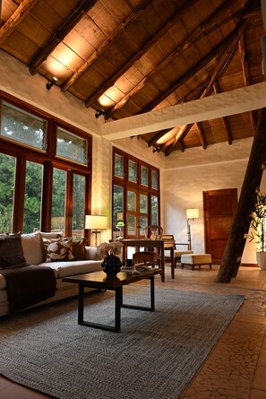 A spacious living room with a high wooden ceiling, large windows, a sofa, a coffee table, and a lamp. - Heated Pool - 4 bedroom Cottage , Pool Table (Provincia de Panamá Oeste)