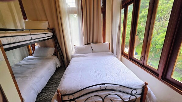 A dormitory-style room with bunk beds and a single bed, large windows with a view of greenery, and curtains. - Heated Pool - 4 bedroom Cottage , Pool Table (Provincia de Panamá Oeste)
