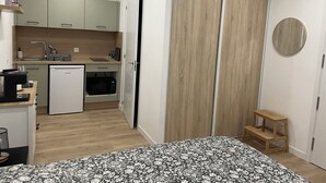 Et kompakt soveværelse med seng, en lille træskammel og et garderobeskab med spejl.