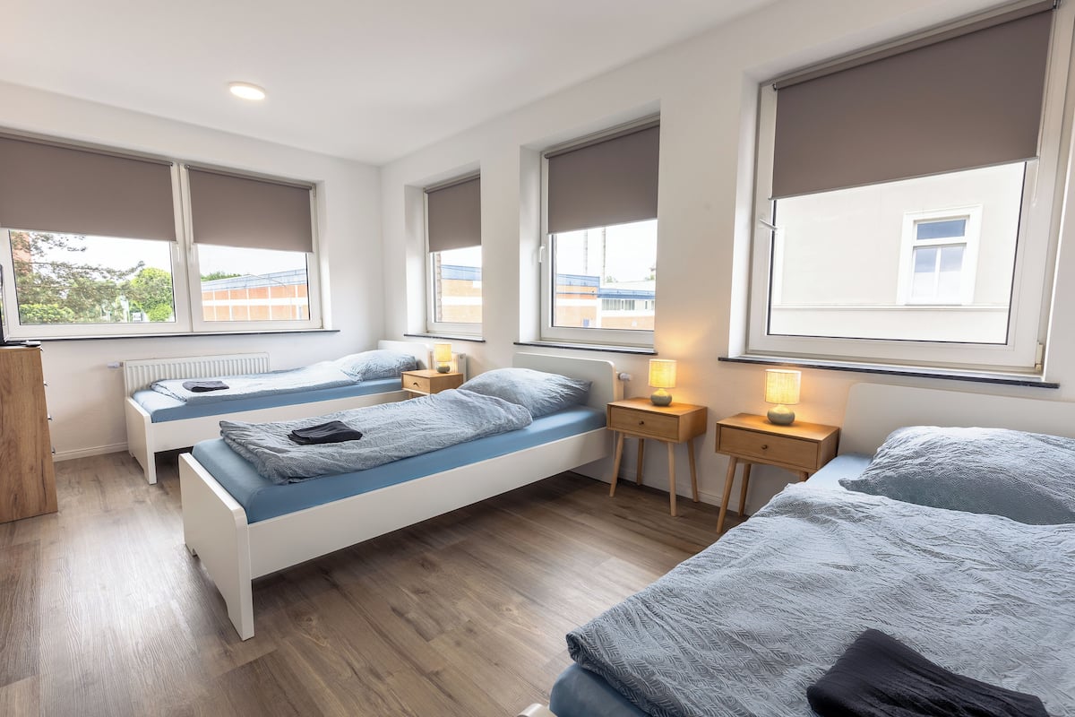 Un dormitorio moderno con dos camas individuales, piso de madera y ventanas grandes con persianas.