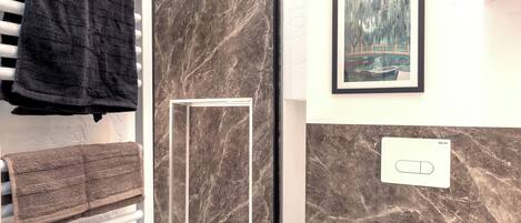 A modern bathroom with a glass shower enclosure, a white toilet, and a towel rack with black towels.