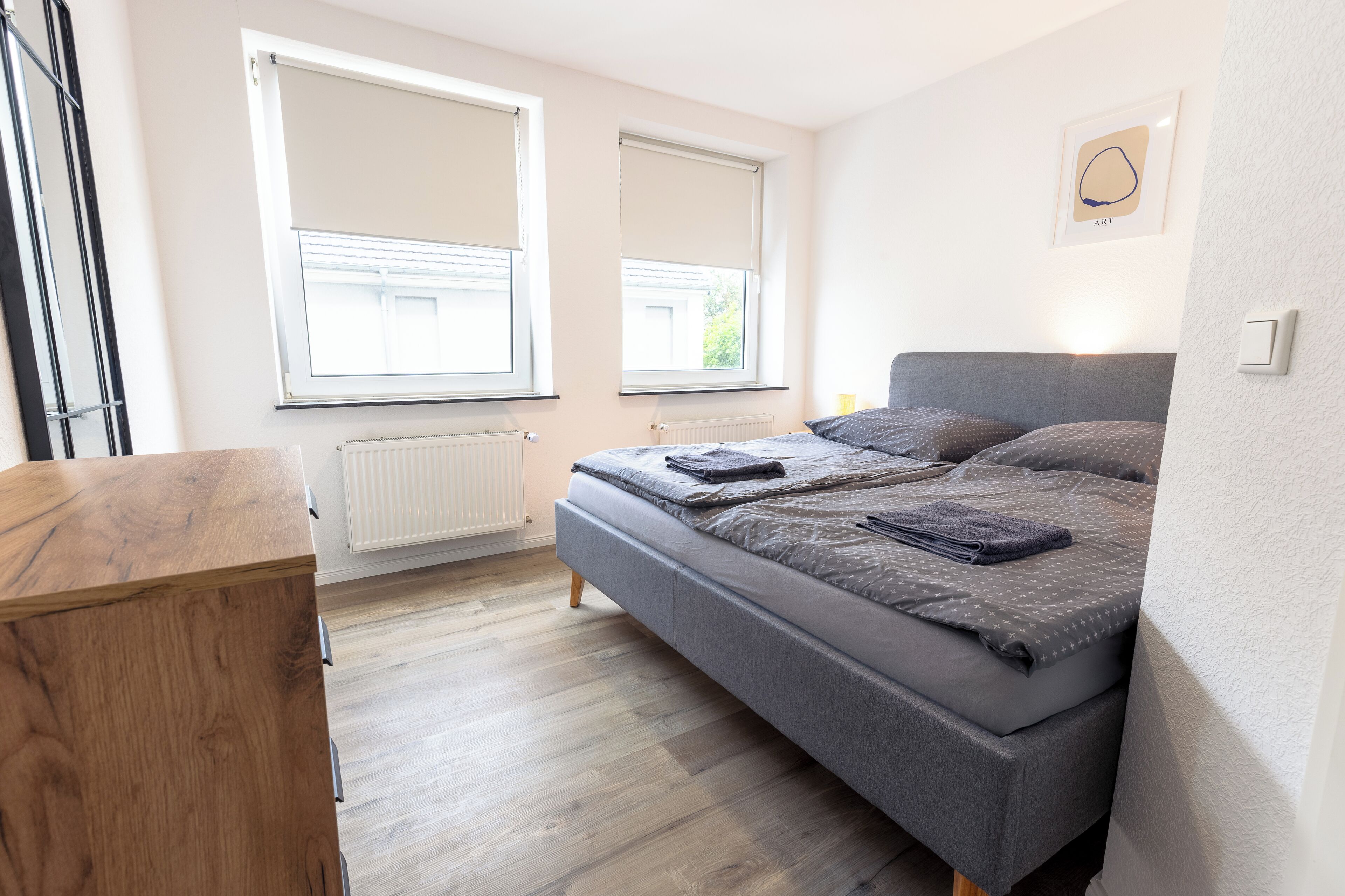 Un dormitorio con una cama, un aparador de madera y dos ventanas con persianas.