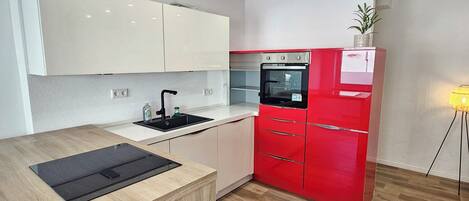 A modern kitchen with white and red cabinetry, a black countertop, and a built-in oven.