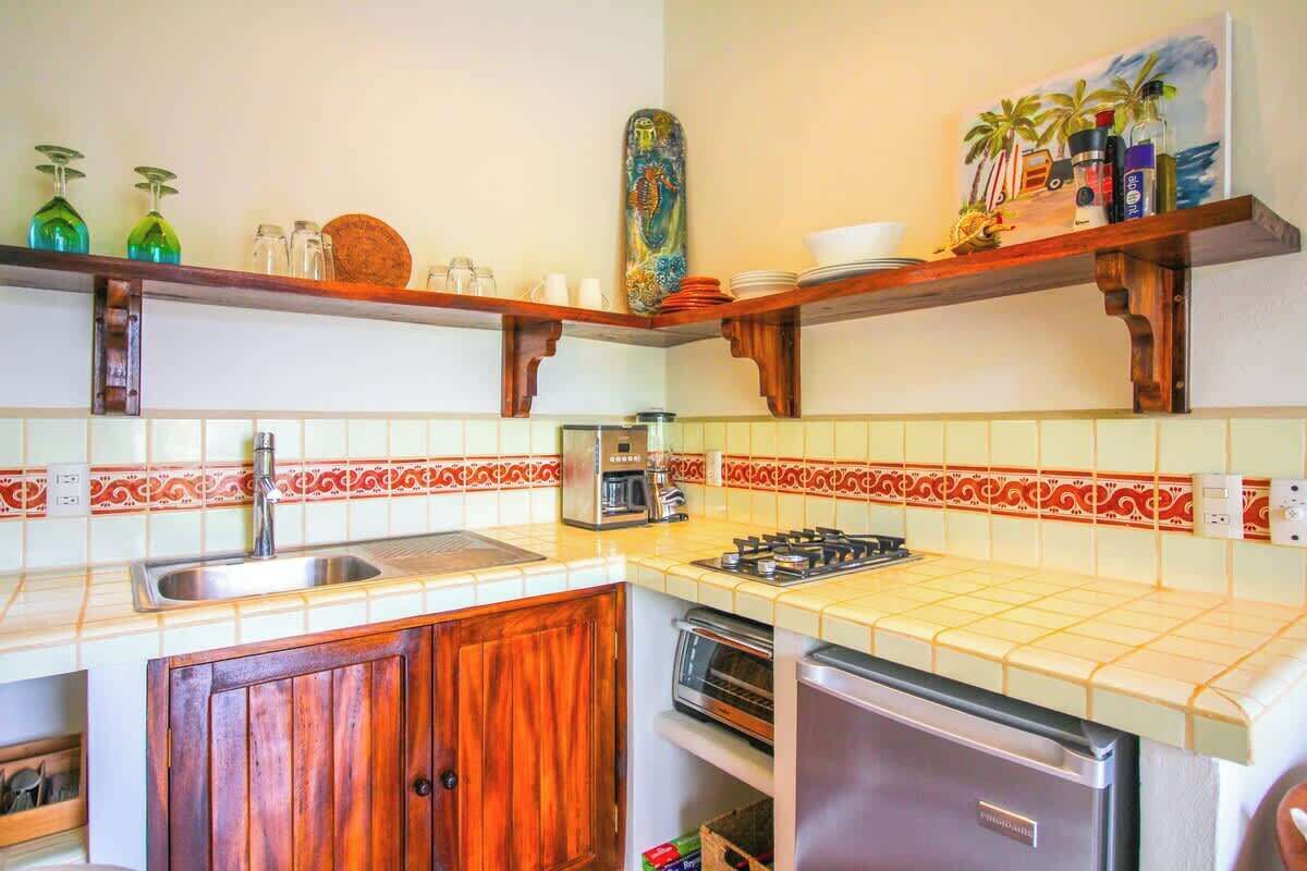 Cocina con lavamanos, estufa y refrigerador. Cuenta con gabinetes de madera y salpicadero de azulejos.