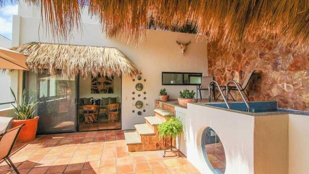 An outdoor patio with a thatched roof, a stone wall, and a pool area.