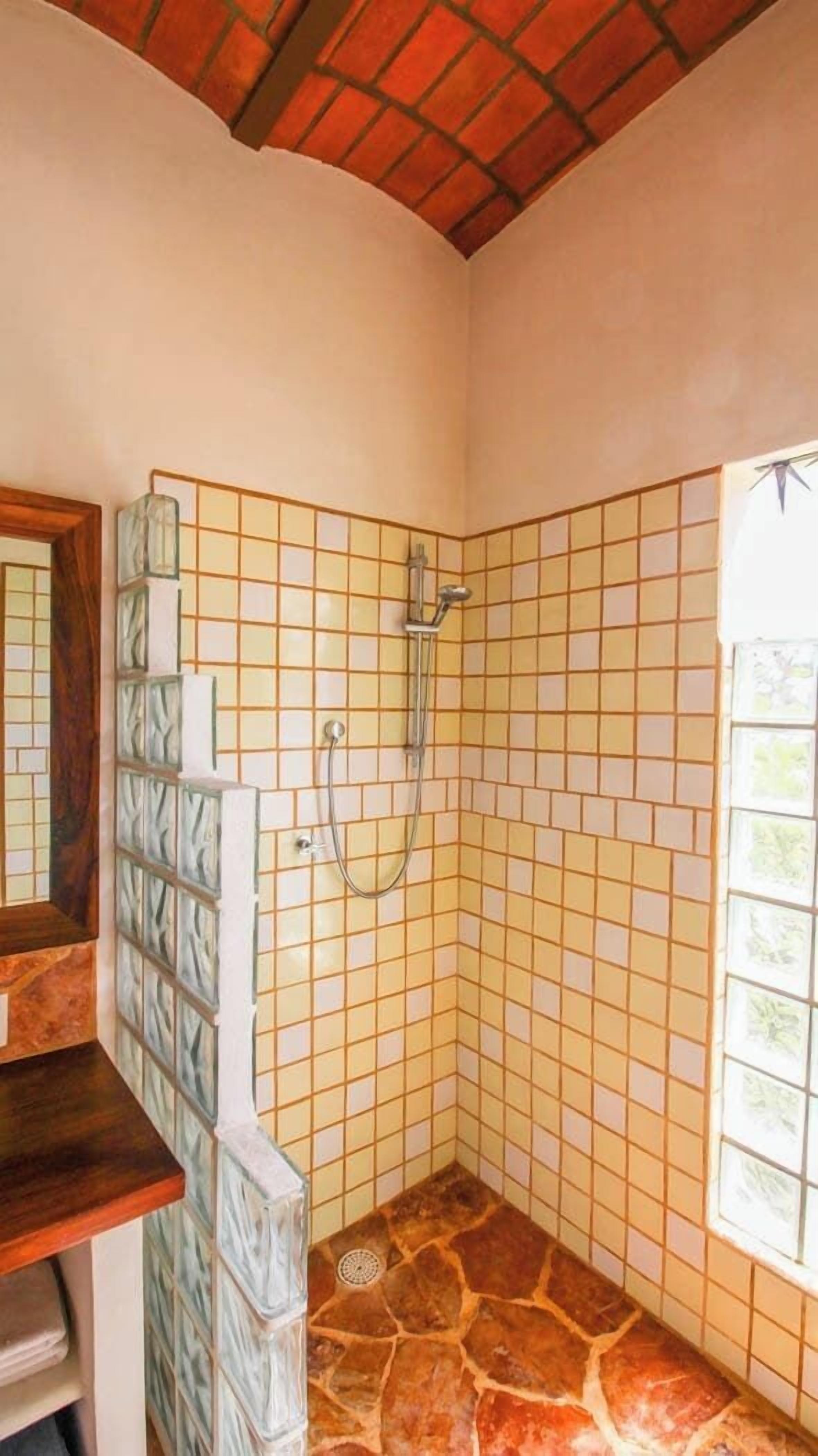 A bathroom with a shower, tiled walls, a wooden ceiling, and a window.