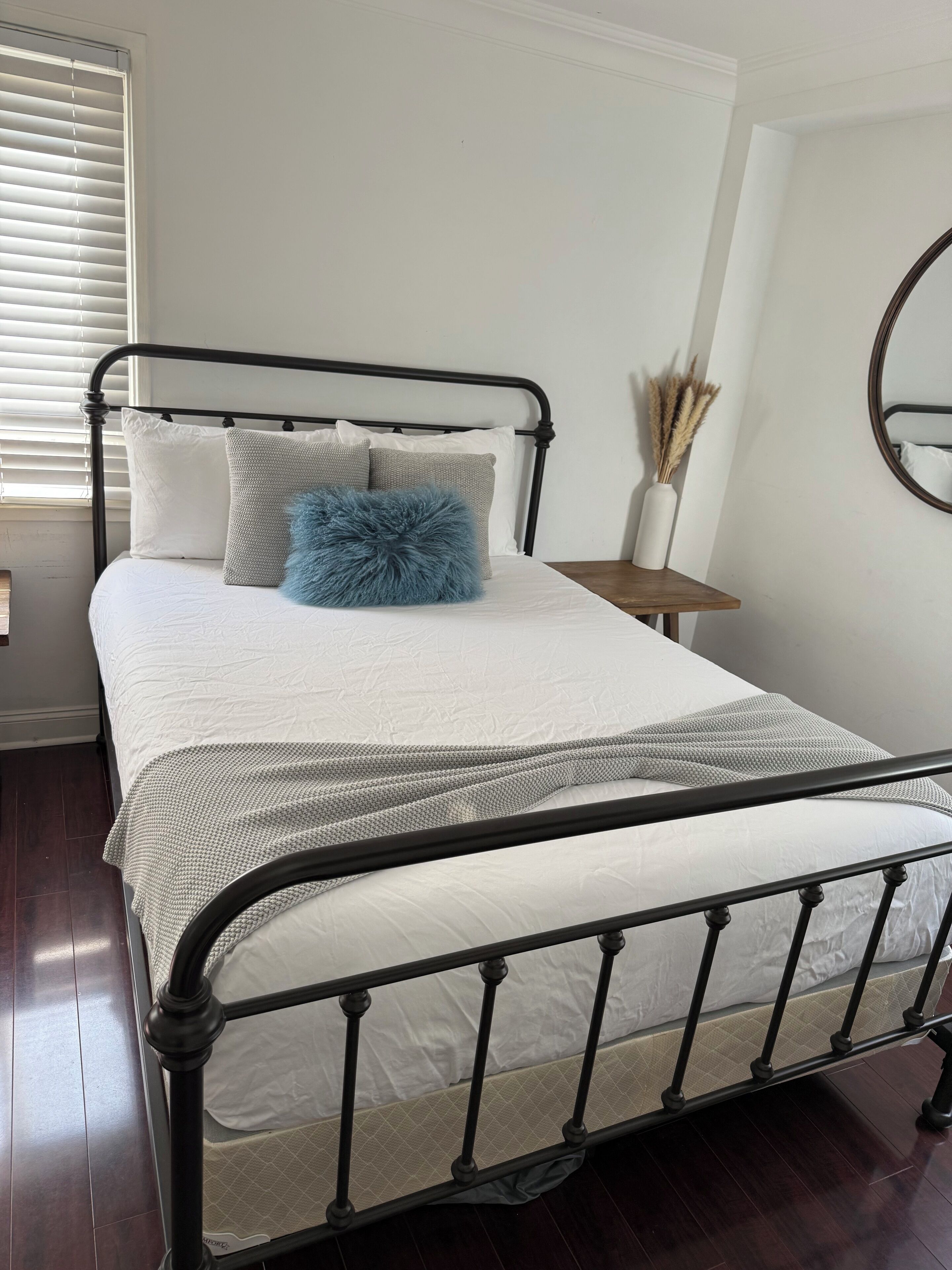 A neatly made bed with a black metal frame, white bedding, and a blue fluffy pillow.