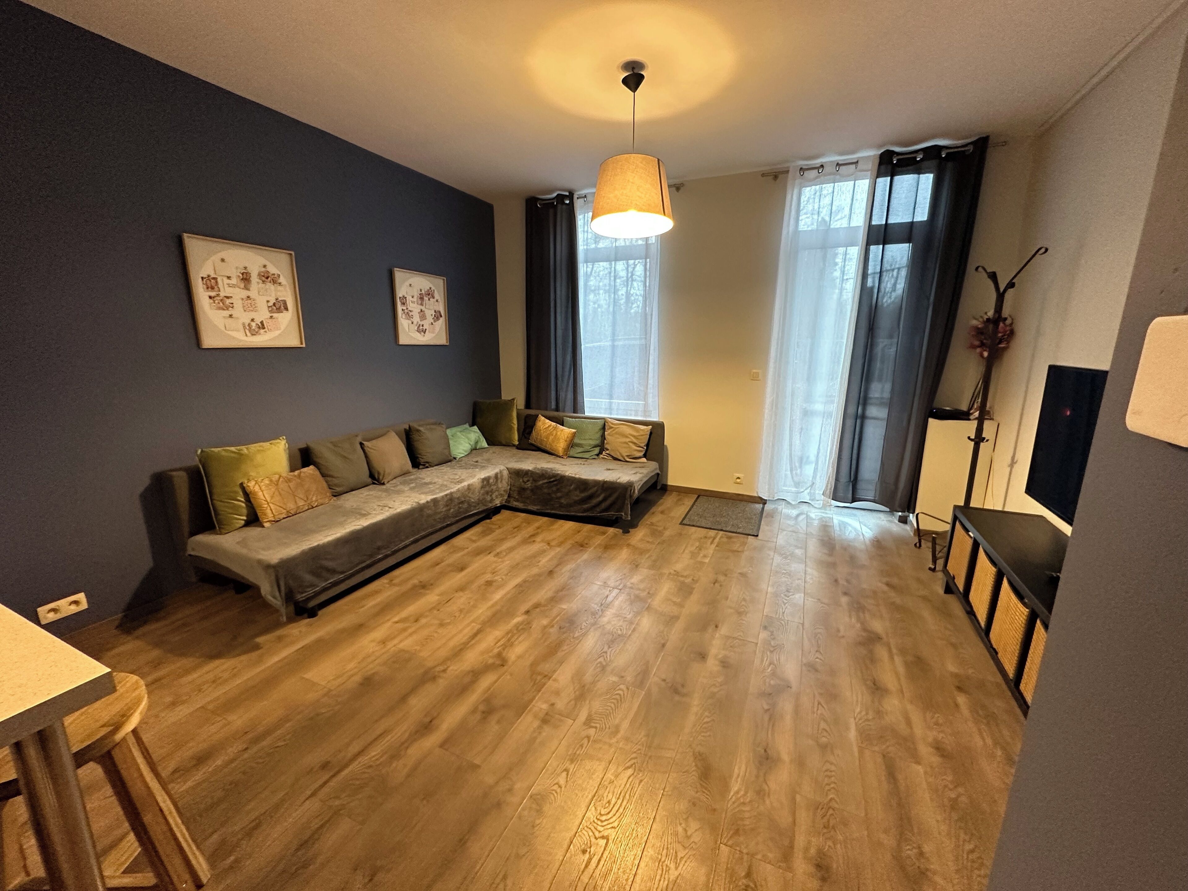 A living room with a sectional sofa, wooden flooring, a ceiling light, and two framed pictures on the wall.
