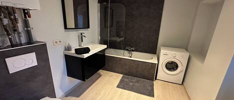 A modern bathroom with a toilet, sink, shower, and washing machine.