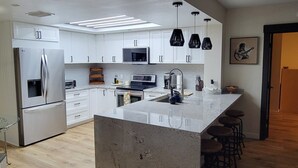 A modern kitchen with white cabinetry, stainless steel appliances, and a central island with bar stools. - Remodeled 2-bedroom condo in serene Sand Key, Clearwater Beach (Clearwater)