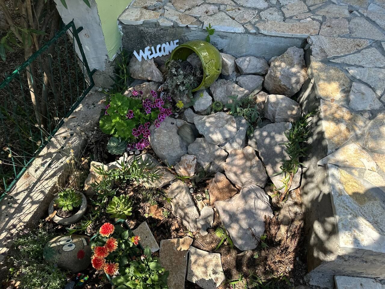 A garden with a welcome sign, rocks, and various plants.