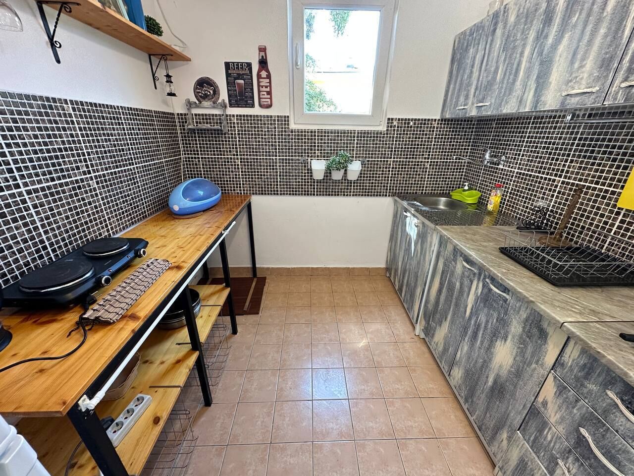 Une cuisine avec un mur recouvert de carreaux, une table en bois, un bol bleu et une fenêtre.