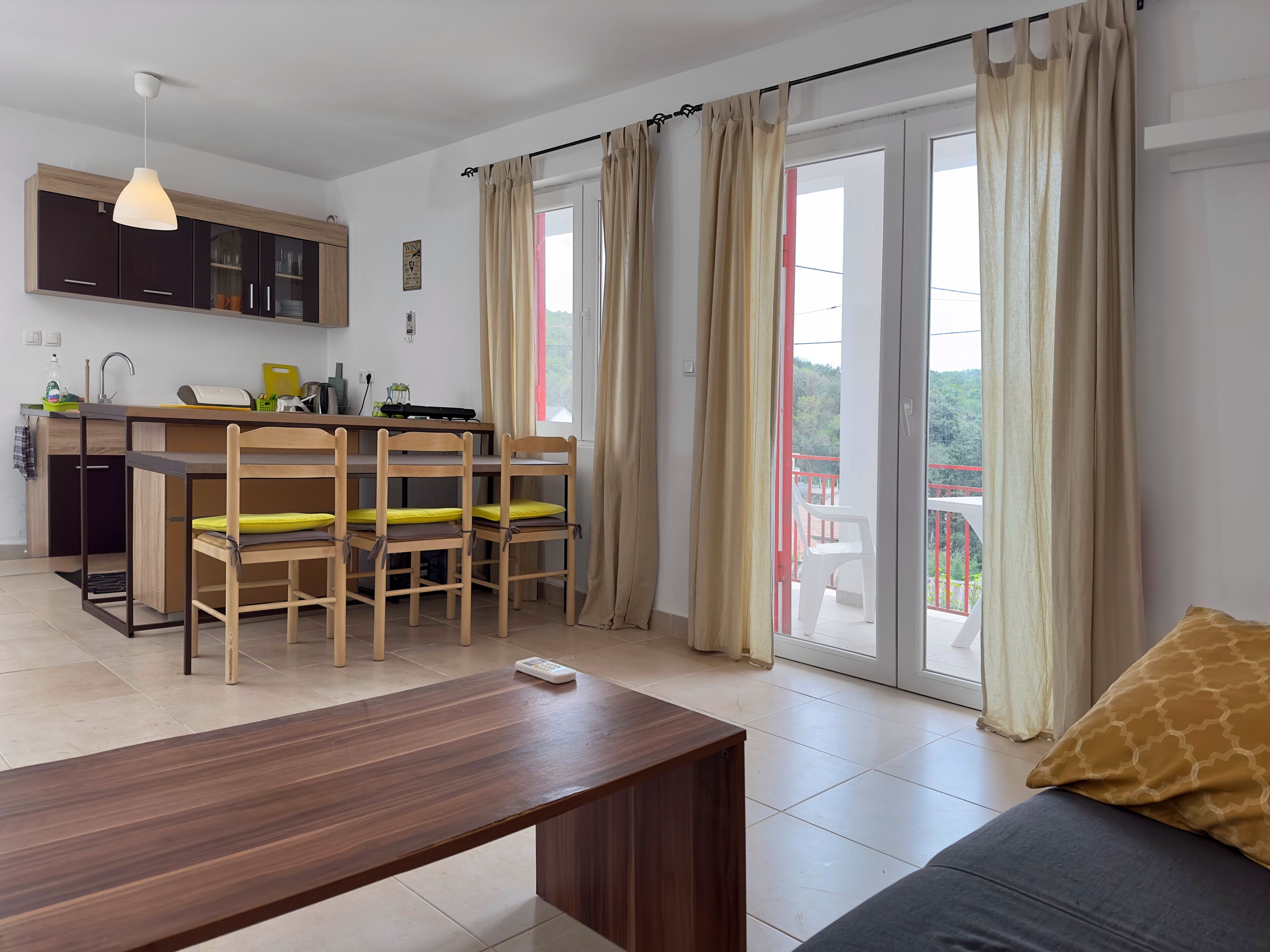 A modern kitchen with dark cabinets, a wooden dining table, and a sofa with a patterned cushion.