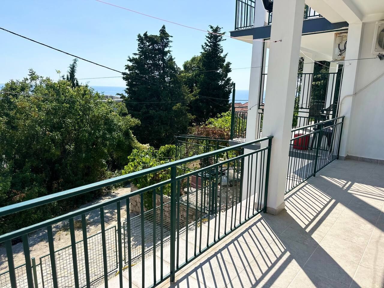 A balcony with a metal railing overlooking a street, trees, and a clear sky.