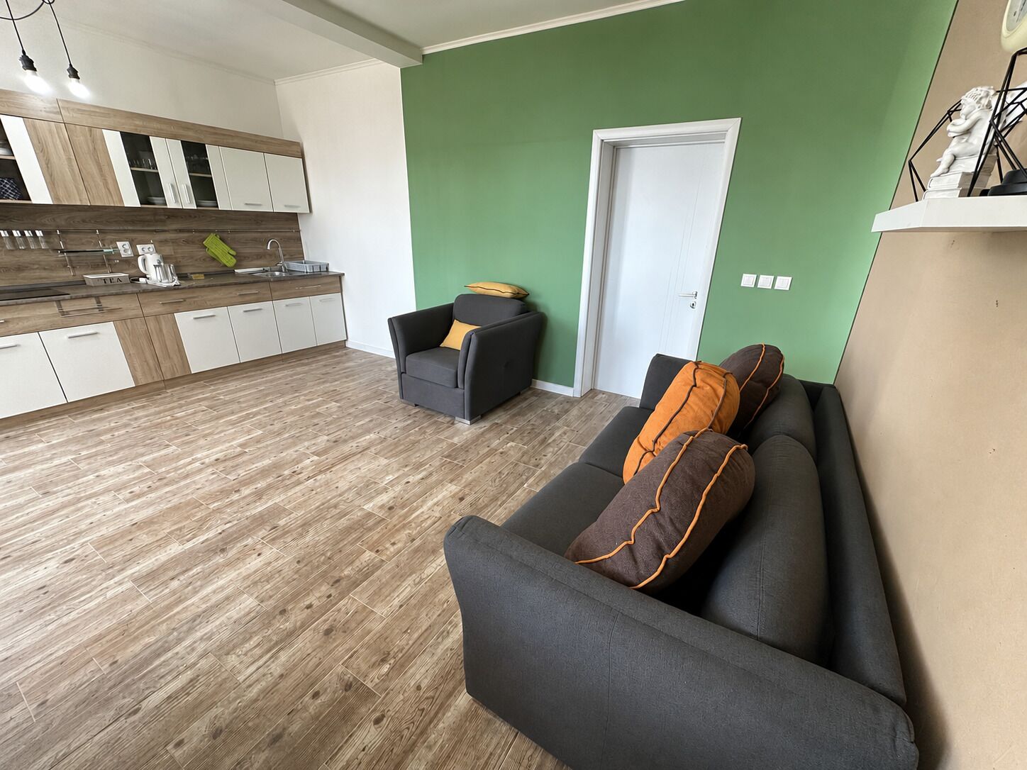 Un salon moderne avec un canapé gris, un petit fauteuil et un mur d’accent vert.