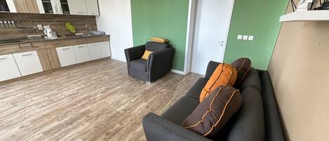 Un salon moderne avec un canapé gris, un petit fauteuil et un mur d’accent vert.