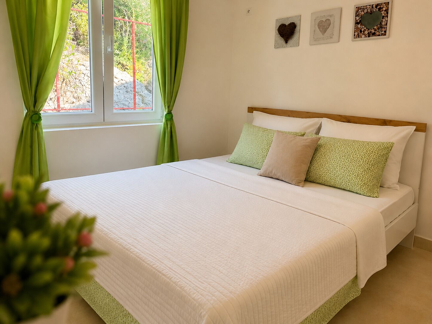 A neatly made bed with a white quilt, green patterned pillows, and a wooden headboard.