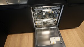 Un lave-vaisselle ouvert dans une cuisine dont le plan de travail est en acier inoxydable et le sol en bois.