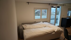 Une chambre à coucher comprenant un lit, une chaise, une fenêtre et une porte donnant sur un balcon.