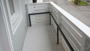 Un balcon doté d’une balustrade blanche, d’un plancher en bois et offrant une vue sur une rue résidentielle.