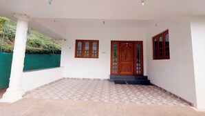 Un espacio exterior techado con suelo de baldosas, pared blanca y puerta de madera con paneles de vidrio.