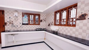 Una cocina moderna con encimera negra, azulejos blancos y un lavamanos empotrado. Se observan ventanas con marcos de madera y un calentador de agua en la pared.