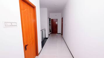 A hallway with a wooden door on the left, a white wall with a light switch, and a tiled floor.