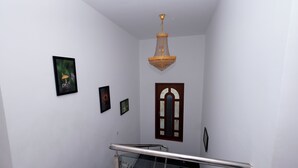Una escalera con barandilla de cristal, un candelabro y cuadros en las paredes.