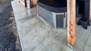 Un área moderna de hidromasaje al aire libre con vigas de madera, suelo de hormigón y una bañera de hidromasaje negra.