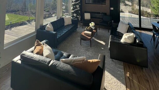 Una sala de estar moderna con ventanas amplias, un sofá modular, una mesa de centro y un televisor de pantalla plana.