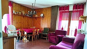 A room with wooden walls, a dining table with chairs, a purple sofa, and a window with curtains. - Casa del sole Oulx vicino alle piste da sci (Oulx)