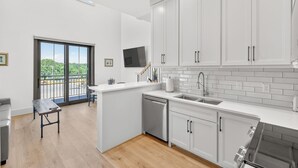 A modern kitchen with white cabinetry, a dishwasher, and a large window with a view of greenery. - New Luxury Condo in The Heart of Nolensville (Nolensville)