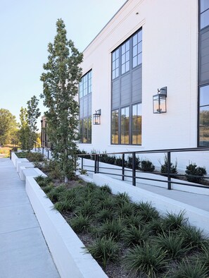 A modern building with large windows, a white exterior, and a landscaped area with plants and a tree. - New Luxury Condo in The Heart of Nolensville (Nolensville)
