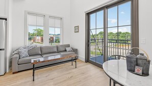 A modern kitchen with a grey sofa, a wooden coffee table, and a large sliding glass door leading to a balcony. - New Luxury Condo in The Heart of Nolensville (Nolensville)