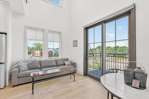 A modern kitchen with a grey sofa, a wooden coffee table, and a large sliding glass door leading to a balcony. - New Luxury Condo in The Heart of Nolensville (Nolensville)