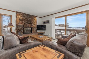 A cozy living room with a stone fireplace, leather sofas, a wooden coffee table, and a TV. - Slopeside Condo|Hot Tub|Free shuttle|Mountain View (Steamboat Springs)
