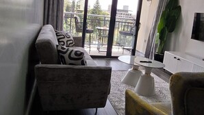 Ein modernes Wohnzimmer mit Sofa, Sessel und einem kleinen Tisch. Ein großes Fenster bietet einen Blick ins Freie.